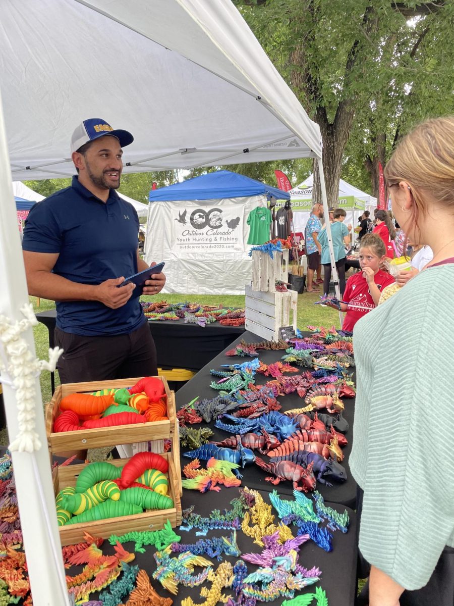 The owner of HQ-PRINTS talks to customers about their products. This booth sold 3D-printed dragons, axolotls and sensory slugs at the Harvest Festival.