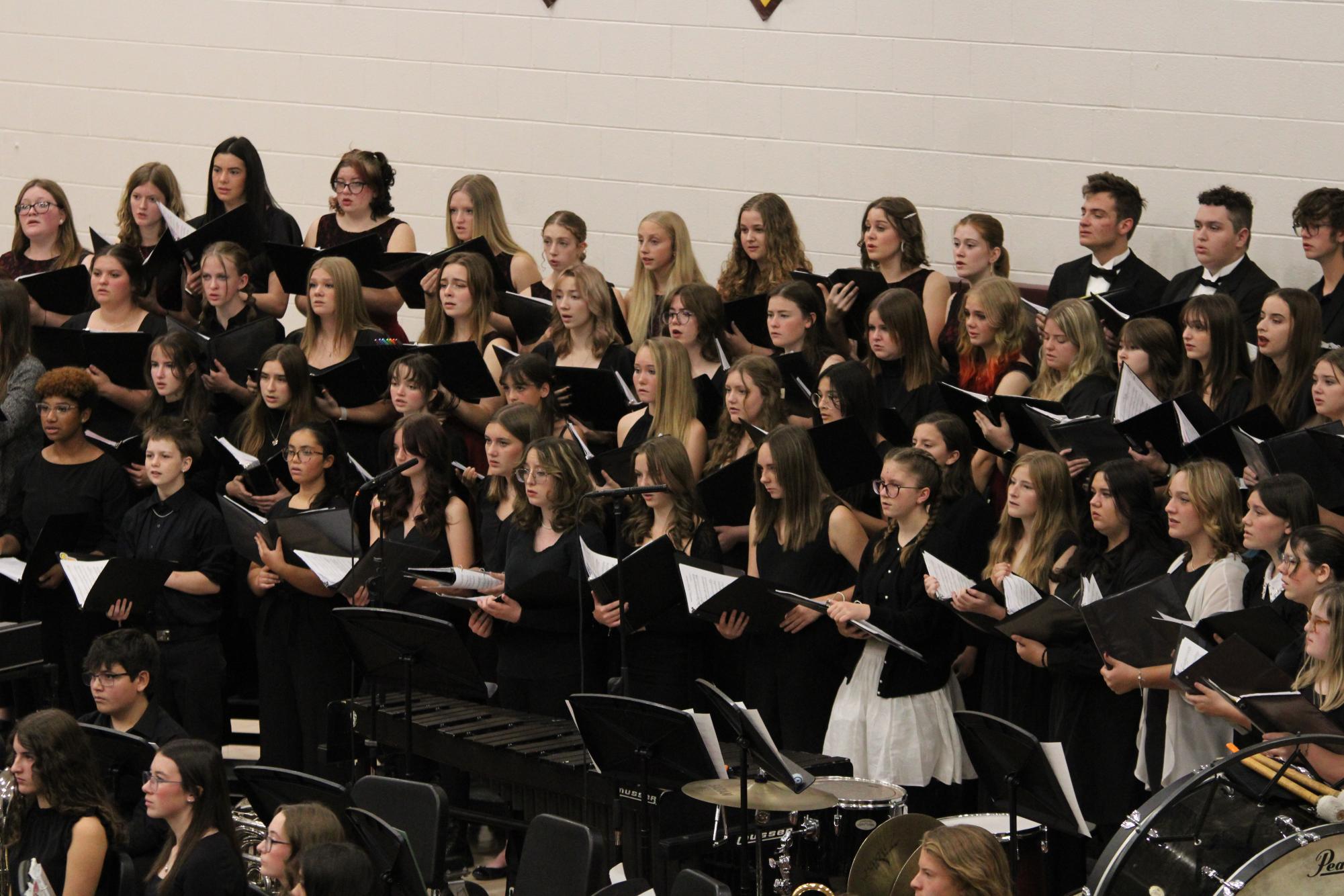 Choir performers stand on the risers, holding black binders of music during the assembly. The songs they sang included In Flanders Fields, Star Spangled Banner and the Armed Forces Medley.