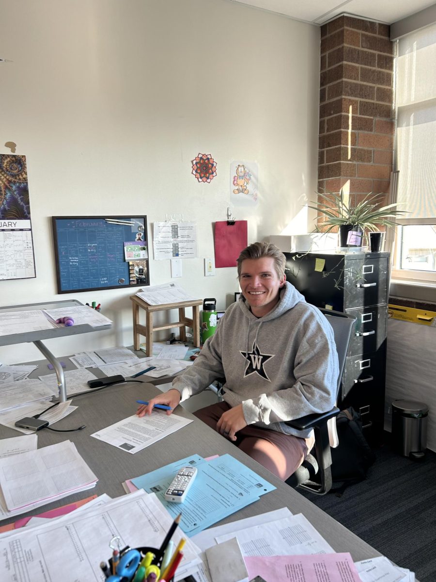 Trevor Wynn (staff) smiles while sitting at his desk. Wynn, other teachers and Matthew Annable (12) provided tips for students to prepare for the SAT.