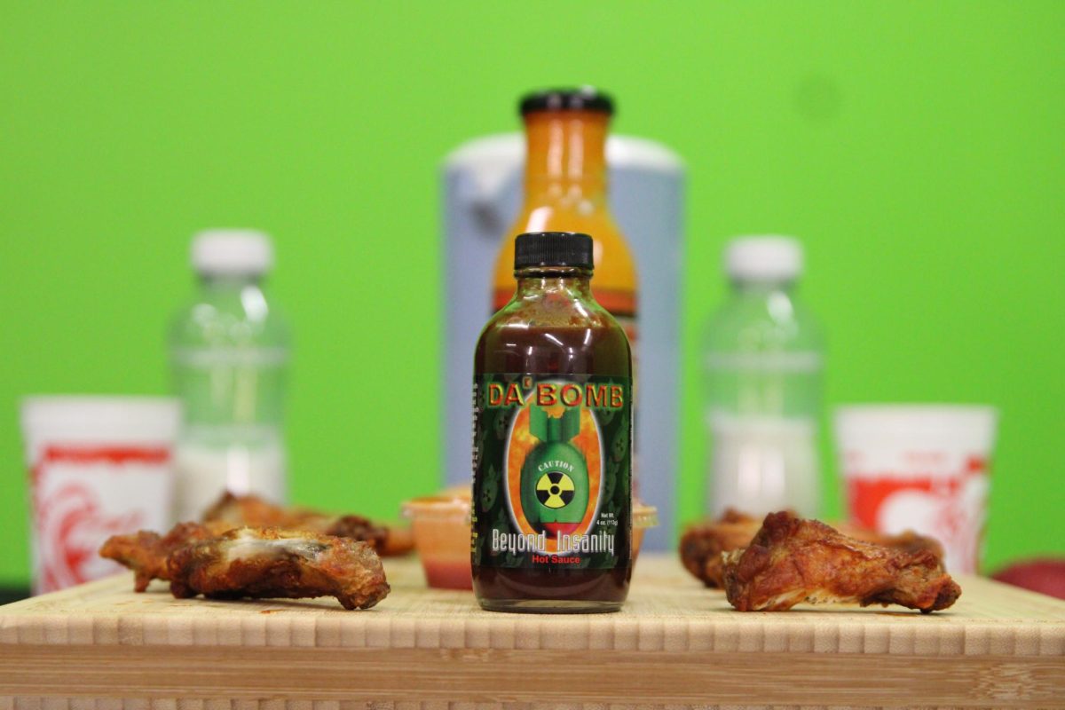 "Da Bomb" hot sauce on a cutting board with wings on either side of it.