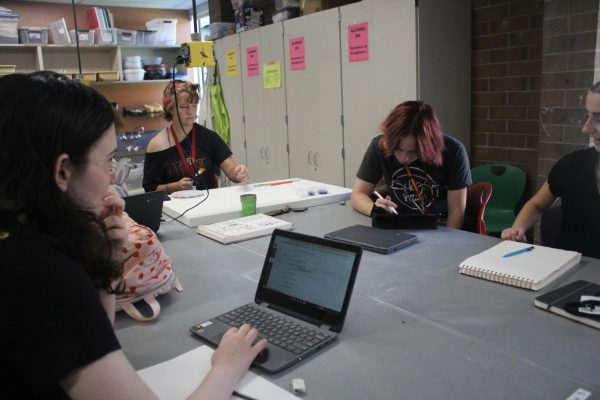 Students sit at art table and work 