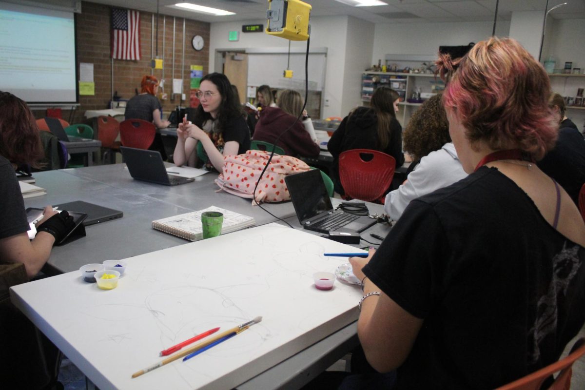 Students sit at art table and work on projects