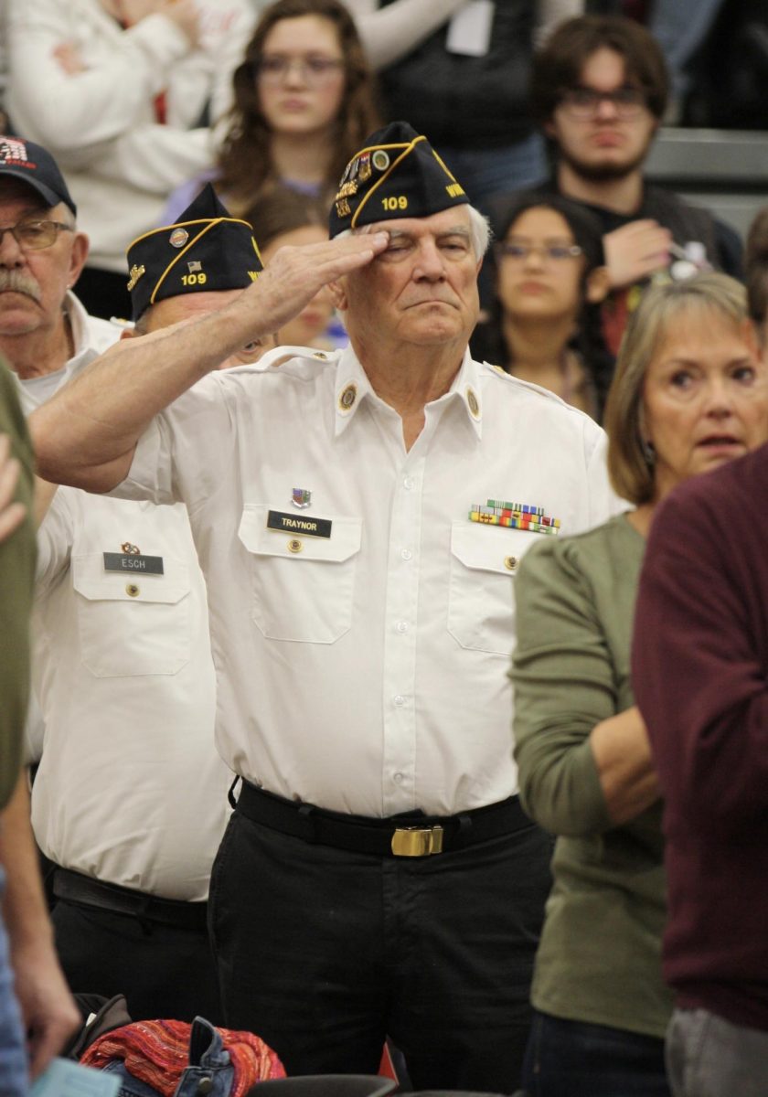 A veteran rises and salutes at the beginning of the assembly. He and many others stood as the National Color Guard presented the colors to the audience.