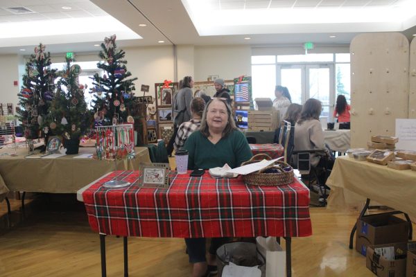 Woman sits at a booth with Christmas trees in the background