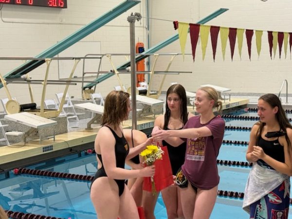 Four swimmers stand and one gives another a gift