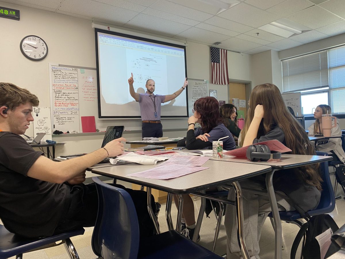 Jeffrey Sesemann (staff) explains an assignment to advanced chemistry students. Sesemann walked around the classroom asking questions to help the students understand. 