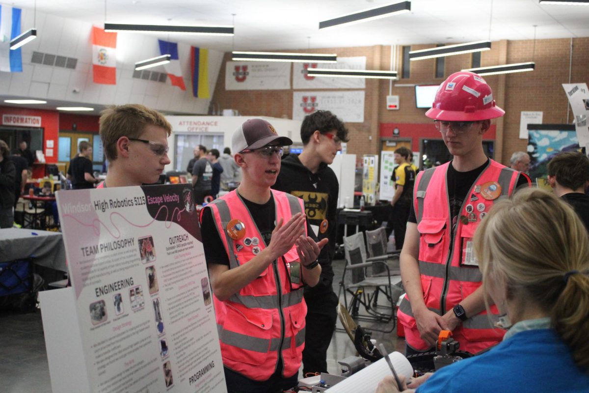 Grady Thorne (12) presents his team's robot to a scoring judge in the pit. "In the pit is just where you hang out for the rest of the day while you're not competing," Camden Timmons (12) explained. "Judges will come around and talk to you, and you will explain about your robot, about your community service and about your outreach."