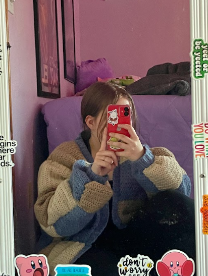 Student takes a selfie in a mirror while wearing a crocheted sweater