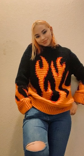 Student stands against a wall and shows off a black sweater with orange flames on it