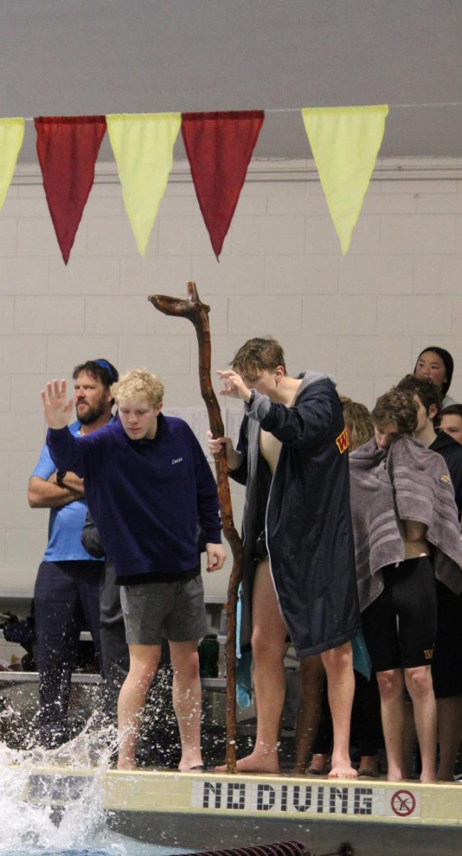 Lucas Penn (11) and Kaden Sanger (12) cheer on their teammate while holding the wizard staff. The staff is a team tradition that is handed down to a swimmer each year. 