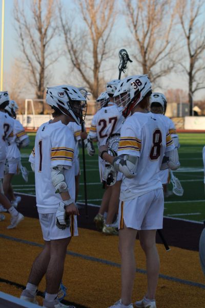 Two lacrosse players stand and talk on the edge of the field